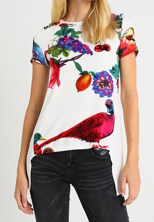 Kurzärmliges weißes Hemd mit lebhaften Drucken von Früchten, Blumen und Vögeln in verschiedenen Farben, kombiniert mit schwarzer Jeans.