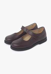 Zapatos Mary Jane de cuero marrón con punta redondeada, bordes festoneados y una correa de Velcro. Suela negra de goma plana y forro interior suave.