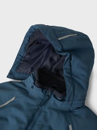 Chaqueta azul con capucha y cremallera, con un collar forrado de forro polar y una franja reflectante en la capucha, exhibida sobre un fondo claro y liso.