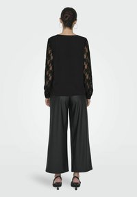 Czarna bluzka z długimi koronkowymi rękawami w połączeniu z wysokimi czarnymi spodniami o szerokich nogawkach. Całość charakteryzuje się luźnym krojem i gładką fakturą.