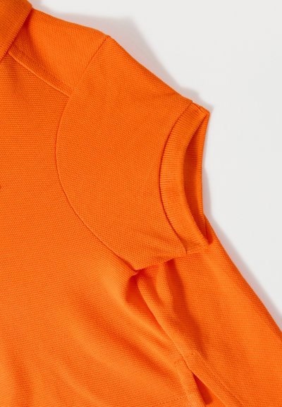Polo à manches courtes orange vif avec poignets de manches côtelés et tissu en maille texturée sur fond blanc.