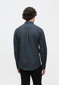 Marineblauw overhemd met knopen, voorzien van een klein wit polkadotpatroon, lange mouwen en een rechte kraag; gladde stoftextuur.