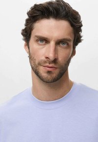T-shirt crewneck di colore viola chiaro con una texture liscia, dotato di maniche corte e dettagli di cucitura minimi, indossato da una persona con capelli scuri.