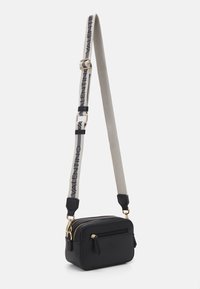 Sac bandoulière en cuir noir avec double fermeture éclair, sangle grise contrastante arborant un logo, quincaillerie dorée et poche à zip à l'avant. Forme rectangulaire compacte.