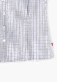 Kortärmad, ljuslila och vit rutmönstrad skjorta med knappar fram, tillverkad av ett mjukt tyg. Lapp på vänster sida synlig.