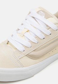 Beżowe trampki Vans z białymi grubymi sznurówkami, zamszową i skórzaną cholewką oraz białą gumową podeszwą, pokazujące zbliżenie na palce i boczną część.