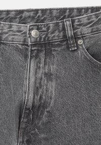 Pantalons en denim gris avec une fermeture à bouton et à fermeture éclair, présentant une finition texturée et des détails de couture visibles le long des coutures et des poches.
