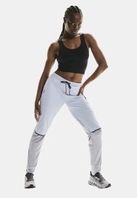 Top deportivo negro y pantalones gris claro con acentos negros. Los pantalones tienen un cinturón ajustable y puños ajustados. Zapatillas en gris y negro.