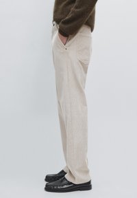 Pantaloni in velluto a coste beige con taglio dritto, tasche laterali e texture sottile; indossati con mocassini neri.