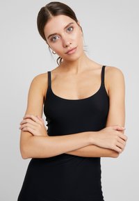 Mustern mustriga mustriga ja õhukeste rihmadega must camisole. Sellel on sile ja keha järgiv disain ning ümar kaelus, valmistatud venivast materjalist.