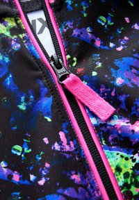 Meer gekleurd sportstof met een zwarte basis, voorzien van een levendig spattenpatroon in blauw, groen en roze, en een roze ritssluiting.