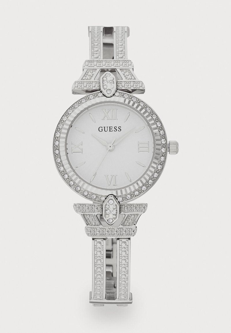 Ceas analog argintiu cu un cadran alb, numere romane, bezel ornamentat și o brățară decorativă cu diamante false și accente geometrice.