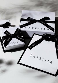 Three white gift boxes of varying sizes, adorned with black ribbons featuring the "LATELITA" logo, on a light surface.