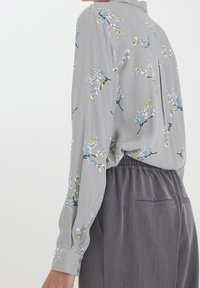 Grijze blouse met lange mouwen en bloemenpatronen in blauw, geel en wit. Lichtgewicht stof met knoopmanchetten en een relaxte pasvorm.