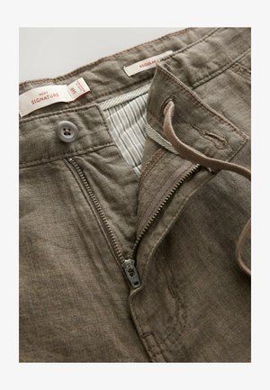 Braune Leinenhosen mit einem Reißverschluss vorne, einem Knopfverschluss und einem gestreiften Innenfutter. Enthält Nähdetails und Etiketten.