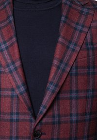 Burgundowa marynarka w kratę z granatowymi akcentami, wykonana z teksturowanej tkaniny. Posiada klapy typu notch oraz pojedyncze zapięcie na guzik, zestawiona z granatowym golfem.
