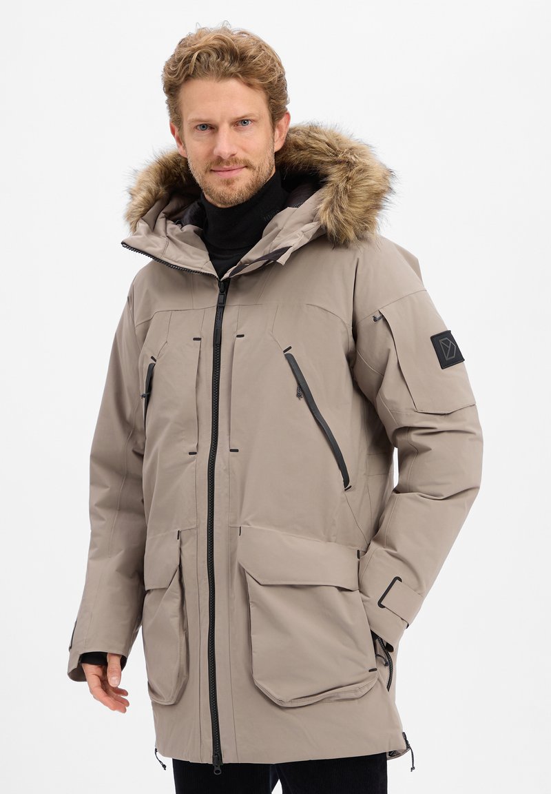 Beige parka met een nepbont kap, voorzien van meerdere rits- en klepzakken, een sluiting met rits aan de voorkant en slanke zwarte accenten. Zachte textuur.