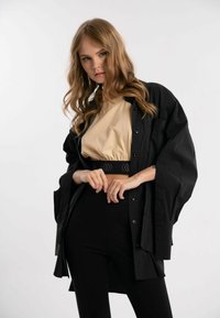 Sort oversized skjorte, beige top, højtaljede sorte bukser. Har knaplukninger, løs pasform og tekstureret elastisk talje med design.