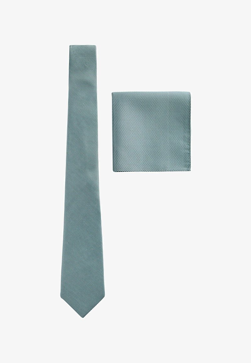 Cravate bleu clair texturée et pochette assortie disposées à plat sur fond blanc.