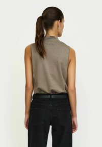 Svijetlosmeđa bezrukavna majica s visokim ovratnikom, teksturirana tkanina, u kombinaciji s crnim hlačama visokog struka koje imaju glatki crni remen.