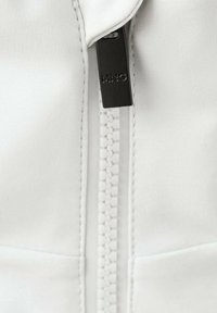 Gros plan d'une fermeture éclair blanche avec une languette noire portant l'inscription "MNG" sur un tissu lisse avec des coutures visibles.