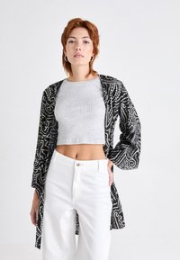 Zwart-wit gestreepte lange cardigan over een grijs crop top, gecombineerd met witte wijde broekspijpen. Glad textuur en een losse pasvorm zijn zichtbaar.