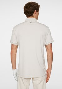 Pikétröja i ljus beige, korta ärmar, mjuk textur och klassisk krage. Har en diskret logotypdetalj på baksidan.