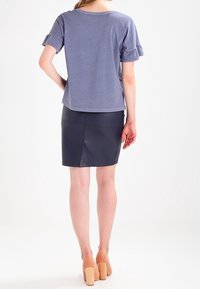 Grå kortärmad topp med volangärmar, tillsammans med en marinblå läderpencilkjol. Modellen bär beige klackskor med blockheel.