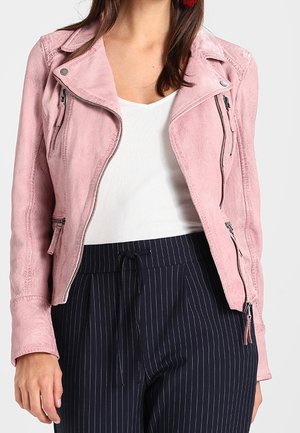 Femme portant une veste biker en daim rose clair par-dessus un top blanc et un pantalon bleu marine à fines rayures avec cordon de serrage.