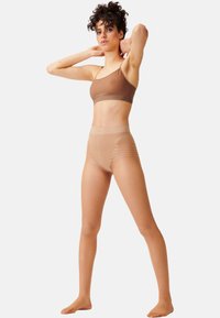 Reggiseno marrone senza cuciture con spalline sottili abbinato a collant trasparenti a vita alta, con una delicata texture a banda e un tono della pelle naturale.