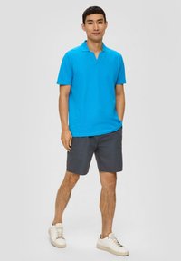 Tropfeneck-Polohemd in Türkis mit kurzem Kragen, kombiniert mit dunkelgrauen Shorts. Tragen mit weißen Sneakern. Einfaches Design und einfarbig.