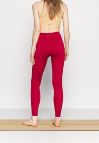 Leggings rossi a vita alta realizzati in tessuto elasticizzato, con una texture liscia e una vita elastica, e un logo sul retro.