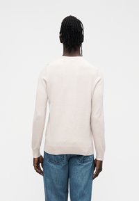 Ljusbeige tröja i mjukt stickat tyg, med långa ärmar, rund halsringning och rak nederkant. Matchas med blå denimjeans.