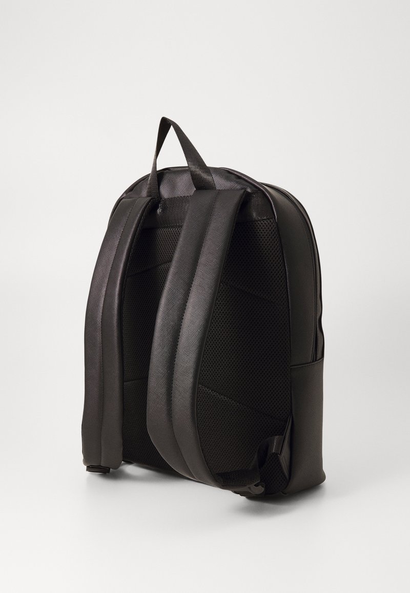 Sac à dos noir en matériau synthétique lisse, avec des bretelles rembourrées, une finition texturée et un design minimaliste sans matériel visible.