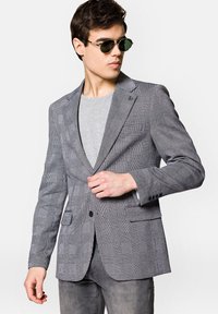 Szary marynarka w kratę wykonana z lekkiego materiału, z klapami notch, zapięciem na jeden guzik i dwiema przednimi kieszeniami. W zestawieniu z szarym t-shirtem.