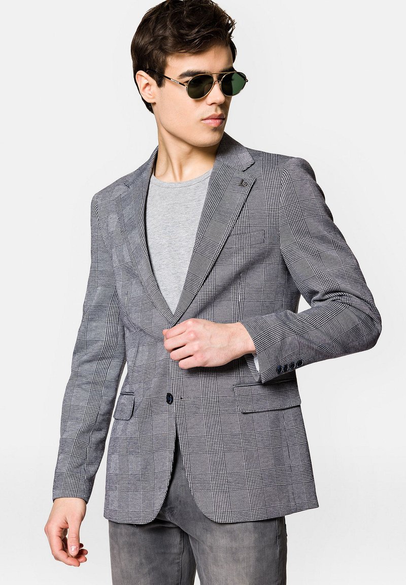 Szary marynarka w kratę wykonana z lekkiego materiału, z klapami notch, zapięciem na jeden guzik i dwiema przednimi kieszeniami. W zestawieniu z szarym t-shirtem.