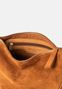 Brown suede handbag interior with a zippered pocket, gold-toned hardware, and embossed "HOLZRICHTER BERLIN" logo on leather.