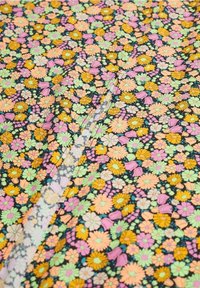 Tejido de algodón floral con margaritas multicolores en rosa, amarillo, verde y morado sobre un fondo negro. Presenta una textura suave.
