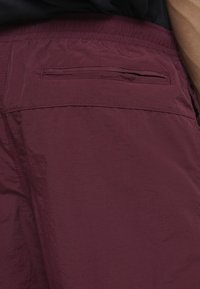 Bordeauxfarbene Shorts mit einer strukturierten Oberfläche, ausgestattet mit einer Gesäßtasche mit horizontalem Öffnen und einem elastischen Bund.