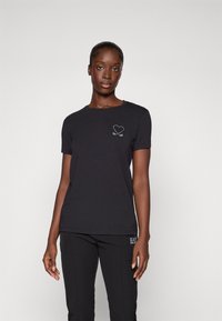 Zwarte katoenen t-shirt met een ronde hals en korte mouwen, met een wit hart en kruisende peddels logo op de borst.