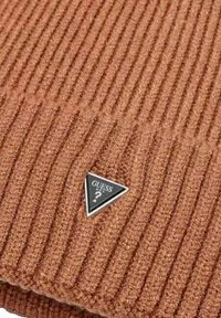Gorro de punto acanalado en un tono naranja óxido con una etiqueta de logo triangular en negro y plateado. La textura parece suave y con relieve.