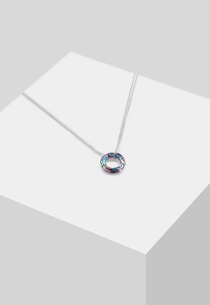 Sølvkæde med et rundt, flerfarvet iriserende vedhæng vist på en hvid geometrisk overflade.