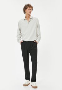 Lys grå skjorte med spread-krave, parret med sorte bukser med elastisk talje og hvide sneakers med beige detaljer.