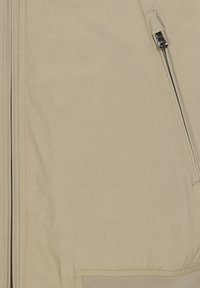 Giacca bomber beige con una texture liscia, chiusura con zip, tasche laterali e orlo a costine. Il tessuto appare leggero e resistente.