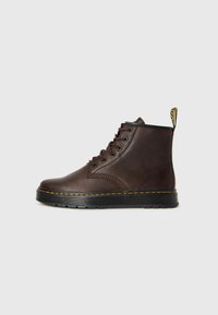 Bottes chevilles en cuir marron avec des semelles en caoutchouc noir, des coutures jaunes et une languette. Elles disposent de lacets ronds et d'un design de bout arrondi et élégant.