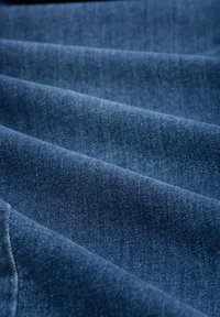 Ciemnoniebieska tkanina z denimu o subtelnej fakturze i lekkim połysku, ukazująca fałdy oraz jednolity wzór splotu. Brak widocznych elementów metalowych lub ozdób.