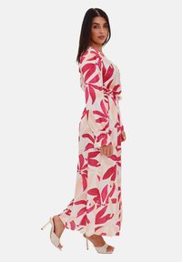 Robe longue et fluide en tissu doux, ornée d'un motif floral dans des nuances de rose et de crème. Manches longues, ceinture à la taille et poignets à volants.
