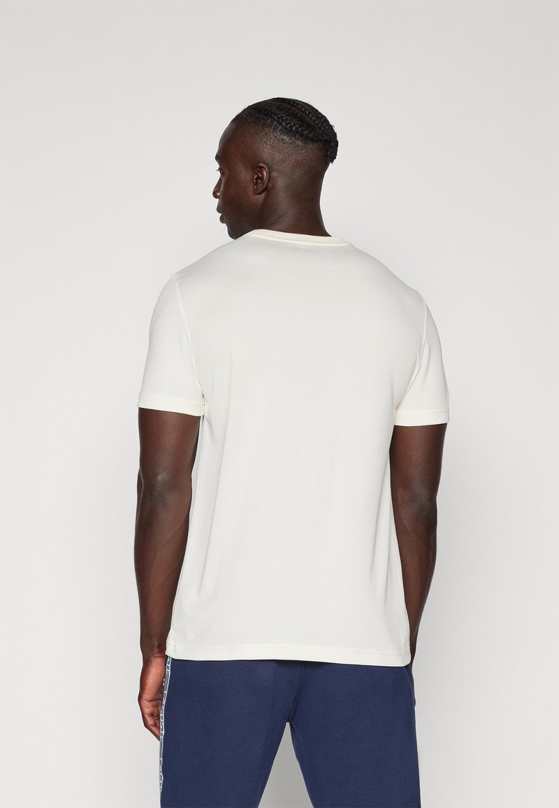 T-shirt crème à manches courtes avec un col rond, texture lisse et coupe décontractée, associé à un pantalon de sport bleu marine.