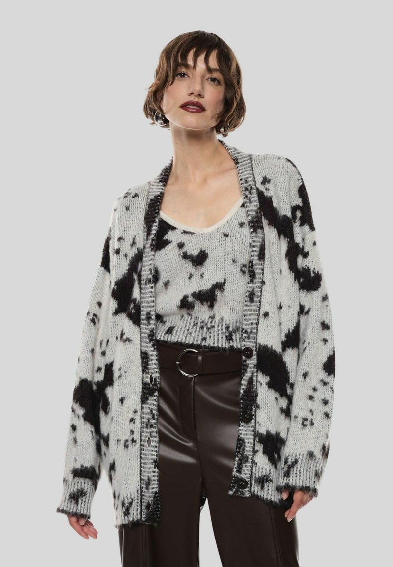 Cardigan tie-dye grigio e nero con una vestibilità morbida, caratterizzato da una texture a costine, maniche lunghe e bottoni grandi. Indossato sopra un top coordinato.