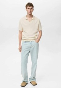Short-sleeve beige knitted polo shirt, light blue straight-leg jeans, and tan slip-on footwear. Simple design with a textured finish.
